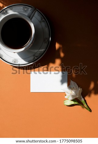 Flat lay of branding identity business name card on a ginger background with a white flower, a cup of coffee, light and shadow. Flat lay, top view. Work, business concept. Home office desk workspace.