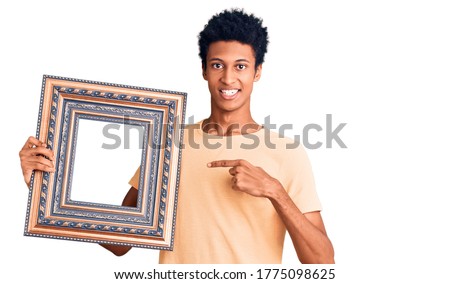 Young african american man holding empty frame smiling happy pointing with hand and finger 