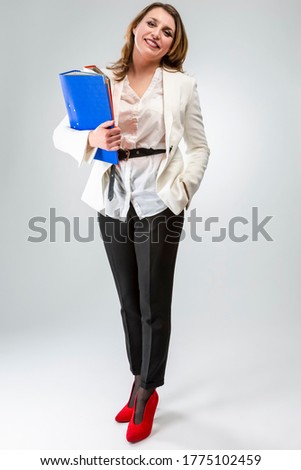 Business Concepts. Full Length Portriat of Positive and Smiling Mature Caucasian Business Woman in White Jacket With Heap of Colorful Folders Against White Background.Vertical Shoot