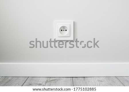 New electrical socket isolated on gray wall. Renovated studio apartment power supply background. Gray wooden floor. Empty copy space white plastic power outlet. Royalty-Free Stock Photo #1775102885
