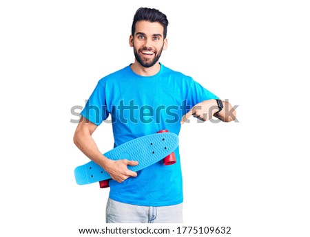 Young handsome man with beard holding skate smiling happy pointing with hand and finger 