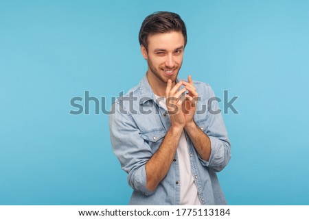 Portrait of cunning cheater, sneaky man in worker denim shirt gesticulating and thinking over devious sly plan of revenge, scheming and conspiring villain plan. studio shot isolated on blue background Royalty-Free Stock Photo #1775113184