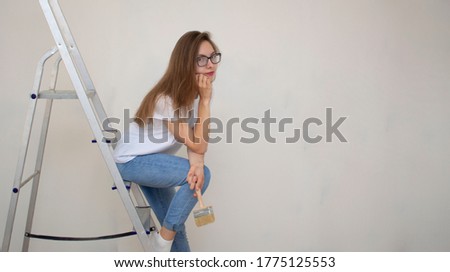 A pensive girl sits on the stairs and looks sadly into a room with an unpainted wall. Repair with your own hands.