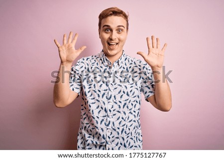 Young handsome redhead man wearing casual summer shirt standing over pink background showing and pointing up with fingers number ten while smiling confident and happy.