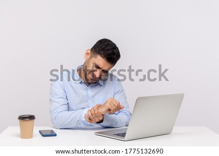 Male employee sitting office workplace with laptop, massaging sore wrist, suffering pinched nerve, stiff muscles, carpal tunnel syndrome after typing on computer. indoor studio shot, white background Royalty-Free Stock Photo #1775132690