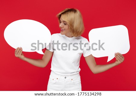 Attractive young blonde woman holding two blanks speech bubbles over red background.