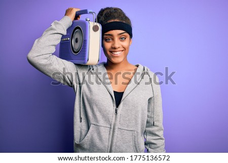 Young african american afro girl listening to music holding vintage radio over purple background with a happy face standing and smiling with a confident smile showing teeth