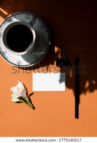 Flat lay of branding identity business name card on a ginger background with a white flower, cup of coffee, pencil, light and shadow. Flat lay, top view. Business concept. Home office desk workspace.