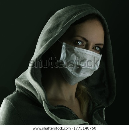 Dark photo of Young serious riot woman wearing medical protactive face mask and hood in the night on black background