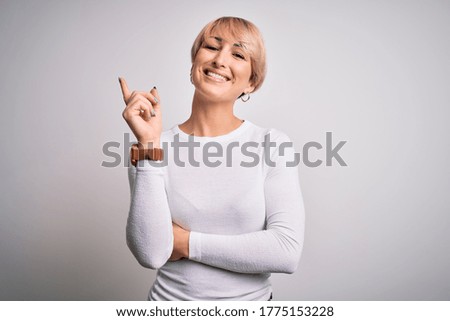 Young beautiful blonde woman with modern short hair hairstyle standing over isolated background with a big smile on face, pointing with hand and finger to the side looking at the camera.