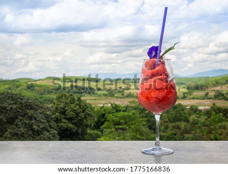 Fresh healthy watermelon smoothie in glass against the background of sky, clouds and mountains. Healthy nutrition and vitamins