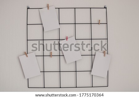 Black metal grid mood inspiration board with mockup empty notes on clamps on a simple white wallpaper background for ideas, organizations, memories, wishlists and photos with  copy space on them.