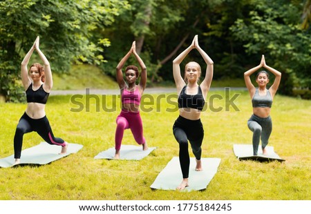 Morning yoga at park. Beautiful girls standing in warrior pose during their outdoor practice. Panorama