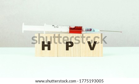 black letters hpv on small wooden cubes and syringe with red vaccine on light green table closeup