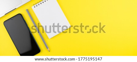 Notepad, pencil, phone and laptop on yellow background. Top view with copy space. Workplace in the office. Flat lay. Mock up.
