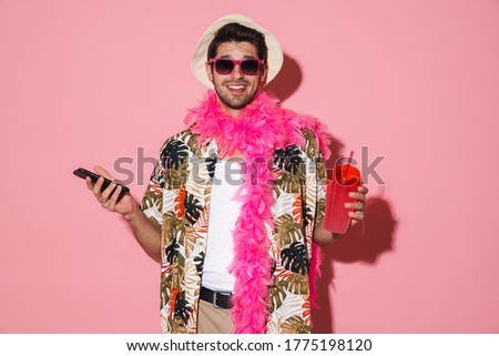 Portrait of smiling man wearing boa using cellphone while drinking soda isolated over pink background Royalty-Free Stock Photo #1775198120