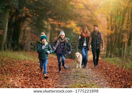 Family Walking With Pet Golden Retriever Dog Along Autumn Woodland Path Together