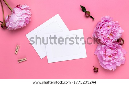 Flat Lay of two white blank paper cards with a pink peonies and clothespins on a pink background.