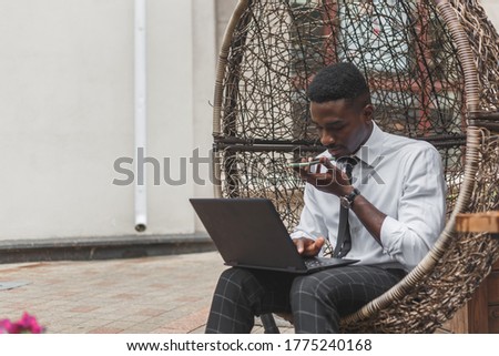 Business african american man holding smartphone, dictating voice message, recording audio, using voice mic. People works outdoors