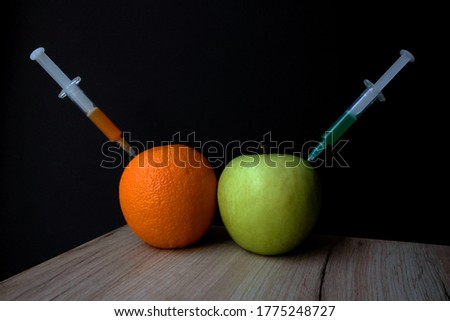 Bright orange and green apple on a wooden board and syringes extracting liquid from them