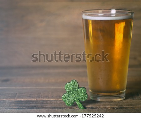 St. Patricks day green shamrock and frosty cold glass of beer on wood background with room or space for text, copy, words.  Vintage camera instagram treatment.