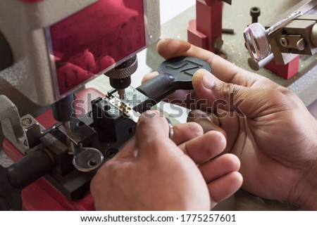 Locksmith in workshop makes new key. Professional making key in locksmith. Machine production of duplicate metal key. Royalty-Free Stock Photo #1775257601