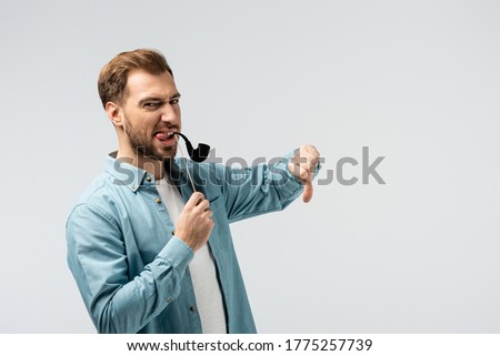 funny young man with fake Tobacco pipe showing thumb down isolated on grey