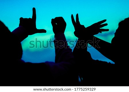 couples hands showing LOVE in silhouette against bluish sky