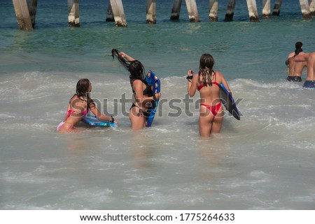 A group of teenage girls with body boards wait for breaking waves.