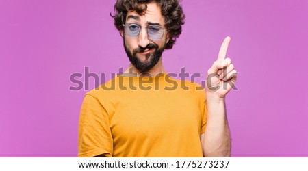 young crazy cool man feeling like a genius holding finger proudly up in the air after realizing a great idea, saying eureka against flat wall Royalty-Free Stock Photo #1775273237
