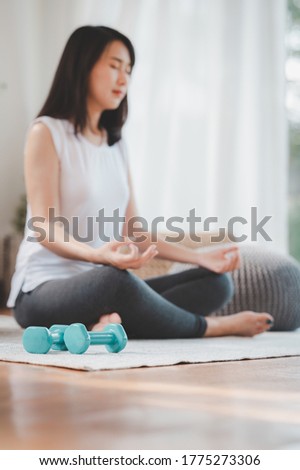 Pair of dumbbell on the living room floor with woman doing yoga meditation in background