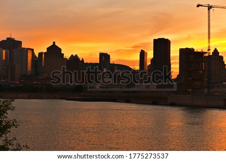 A skyline of a city at the time between sunset and twilight. Reflections of sun rays on a river, Montreal Downtown and Saint Laurent river. Background is Mount Royal. Summer, Spring, outdoors concepts