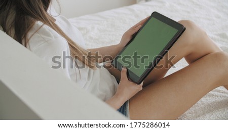 View over head on of caucasian woman lying on the bed at home. Girl holding tablet computer with green screen while watching something. Chroma key