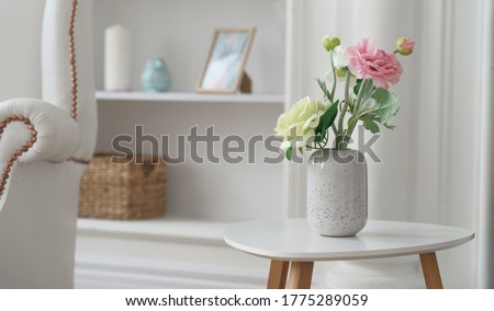 Pink and yellow roses in Modern white vase on white table beside classic armchair Royalty-Free Stock Photo #1775289059
