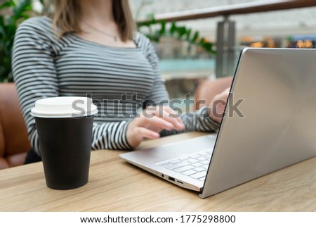 Close up photo ofnotebook being used by young caucasian business woman in a striped jacket sitting at the table. Nearby is a plastic cup of coffee . Business woman Concept. Lifestyle concept.