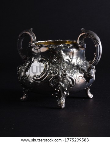 A vintage silver tea set service, photographed on black with a moody atmospheric lighting scene