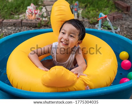 Asian cute child boy laughing while playing water in blue bowl in rural nature. Young kid having happy moment in summer. Family activity at home and preschool concept.