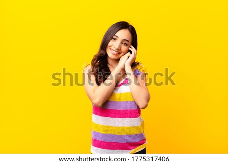 young latin pretty woman feeling in love and looking cute, adorable and happy, smiling romantically with hands next to face against flat wall
