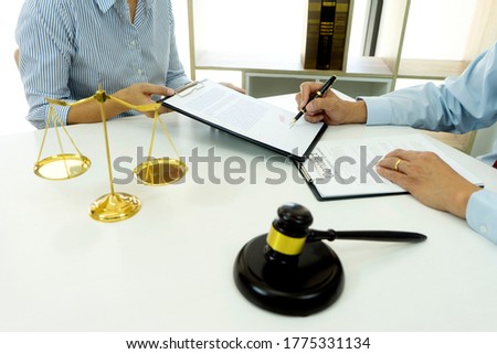 On the table in the lawyer office businessman signature to the contract on the clipboard white copy space with balance and gavel.