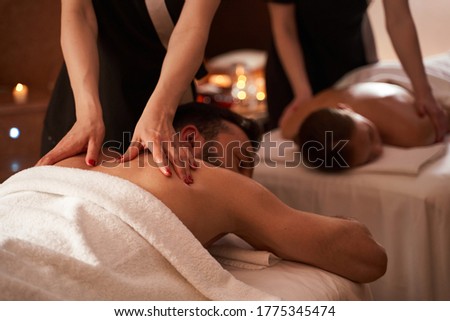 Cropped photo of a professional therapist massaging young man. White towel covering his body