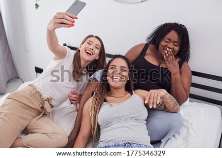 Pleasant smiling Caucasian female shooting photo portrait of herself in company of her Afro American female mates