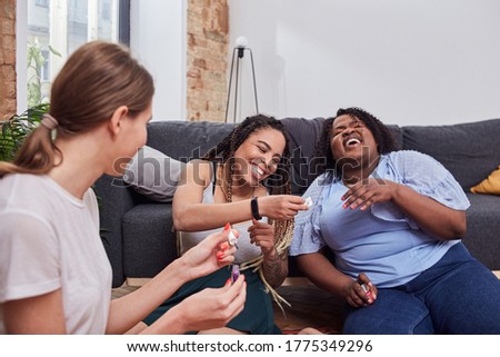 Positive friends laughing uncontrollably while holding polish bottle and coloring their nails Royalty-Free Stock Photo #1775349296