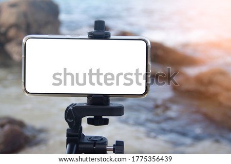 soft sunlight Close-up  Blank white display screen of the smartphone camera stands on a tripod to capture the sea and beach stone