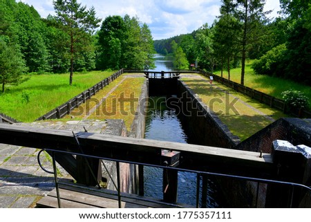 Close up on massive dam doors used to lower or increase water level with a narrow channel with concrete edges seen in the middle of a dense forest or moor on a cloudy summer day in Poland