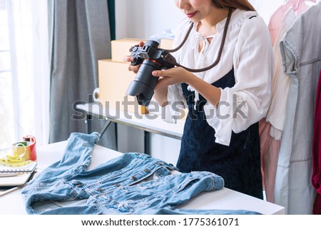 Young Asian entrepreneur using a camera take a photo of product for upload to website online shop. Online selling, e-commerce, business and technology concept.