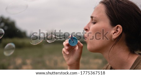 The girl blows soap bubbles. A young woman sits in nature and blows soap balls. Face in profile, side view.