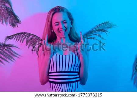 A girl in neon shows a fak on the background of tropical leaves.