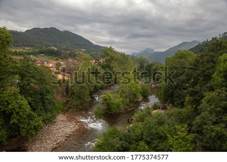 Summer, cloudy day. Mountain river with a village on the shore against the backdrop of the mountains.