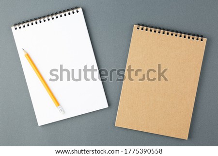 Open notebook with clear page with yellow pencil on grey background. Design business, office supplies or education concept. Ready for adding or mock up. Top view.