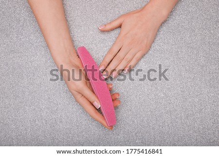 Beautiful female hands with stylish nail manicure gel polish on silver background. Top view. Woman files her nails.